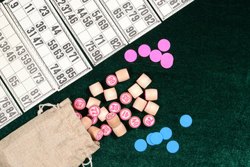 Lotto, classic family board game. Some wooden barrels, blue chips and cards on green velvet surface. Vintage game, bingo.