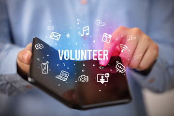Businessman holding a foldable smartphone with VOLUNTEER inscription, social media concept