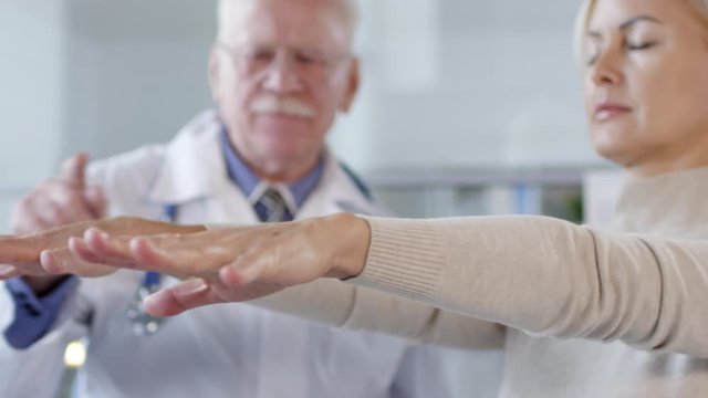 Close up of middle aged caucasian woman standing with eyes closed and then touching nose with finger and clenching fists while senior neurologist speaking to her during proprioception test