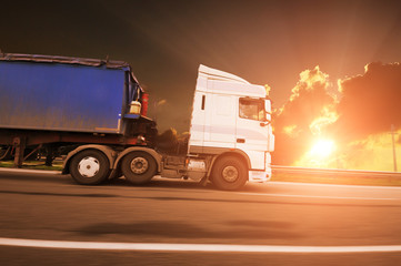 Truck with a trailer in motion on the countryside road against sky with sunset