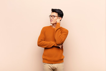 young chinese man with a concentrated look, wondering with a doubtful expression, looking up and to...
