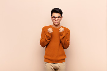 young chinese man looking confident, angry, strong and aggressive, with fists ready to fight in...
