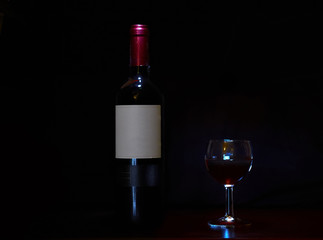 Wine bottle and a glass of red wine against dark background/Bottle of red wine with glass
