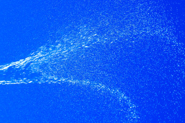Fototapeta na wymiar Blurred in motion jet of water on a blue background. Brilliant spray.