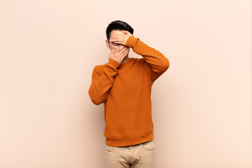 young chinese man covering face with both hands saying no to the camera! refusing pictures or...