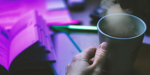 Hands with cup of coffee and phone in office with neon light. Banner background