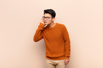 young chinese man looking serious and curious, listening, trying to hear a secret conversation or...