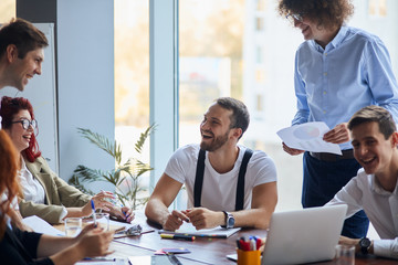 Team of cheerful caucasian business people in smart formal wear sitting together at table and discussing something while laugh and smile. Happy teamwork, co-working
