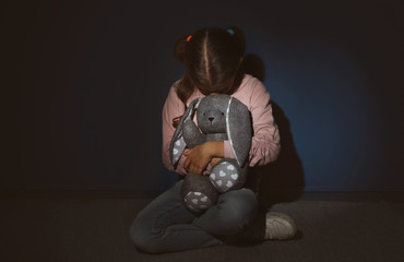 Scared little girl with toy near blue wall. Domestic violence concept