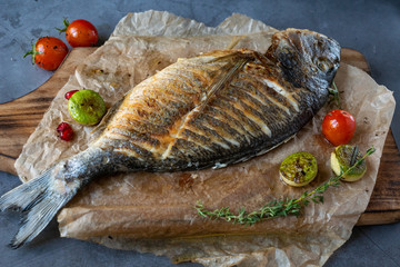 grilled delicious dorada fish with grilled vegetables on wooden plate, tasty food concept