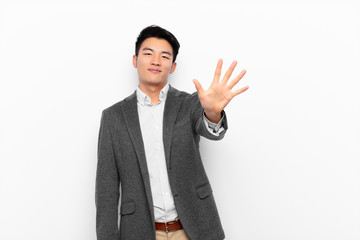 young chinese man smiling and looking friendly, showing number five or fifth with hand forward,...