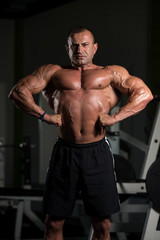 Obraz na płótnie Canvas Muscular Mature Man Flexing Muscles In Gym