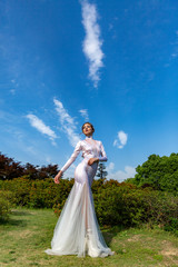 girl in a white long dress on a background of blue sky with white clouds