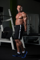 Fototapeta na wymiar Muscular Mature Man Flexing Muscles In Gym