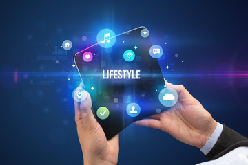 Businessman holding a foldable smartphone with LIFESTYLE inscription, social media concept