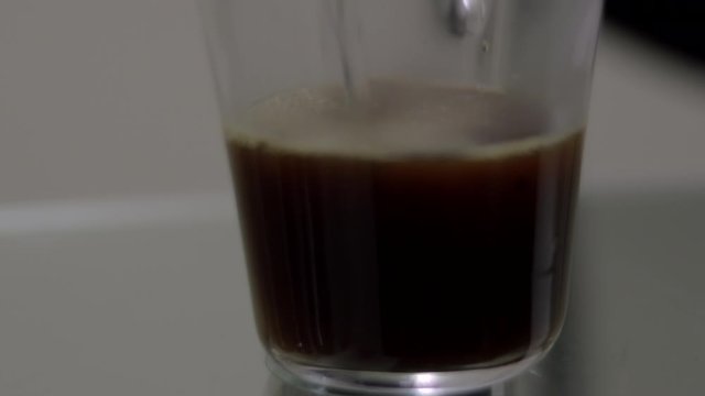 Hot water slowly pours into glass of instant coffee isolated on table