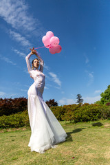 girl in a white long dress with pink balloons on the nature
