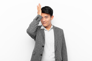 young chinese man raising palm to forehead thinking oops, after making a stupid mistake or...