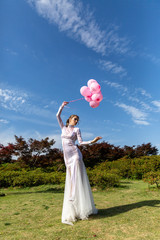 girl in a white long dress with pink balloons on the nature