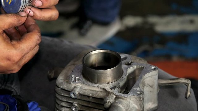 Bike mechanic applying step ring on piston for motorbike. close up