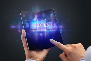 Businessman holding a foldable smartphone with ROBOTICS inscription, new technology concept