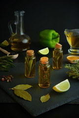 Olive oil, lemon, rosemary, thyme, sweet pepper, lime, bay leaf, peppercorns,. Gastronomy situation with spices and ingredients on a dark background.