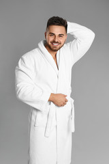 Happy young man in bathrobe on grey background