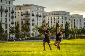 Two young attractive athletes run in the park of a modern city
