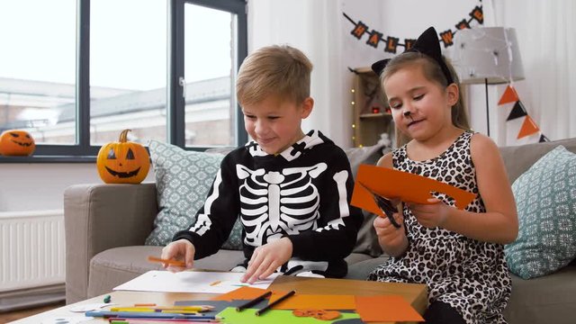 halloween, holiday and childhood concept - smiling little boy and girl in costumes doing crafts at home