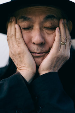 手で顔を覆い、帽子を被ったシニア男性のポートレート