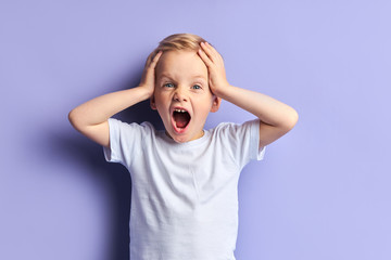 Blond boy screaming, with opened mouth. Wearing white t-shirt, purple background