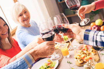 Happy people sitting at home behind table, clinking beverage glasses
