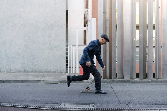 屋外でスケートボードに乗ろうとしている、ハンチング帽を被ったシニア男性のポートレート