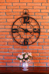 round black clock on brick wall. wooden shelf with a bouquet of