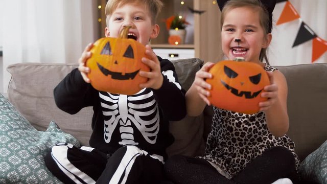 halloween, holiday and childhood concept - smiling little boy and girl in costumes with jack-o-lantern pumpkins having fun at home