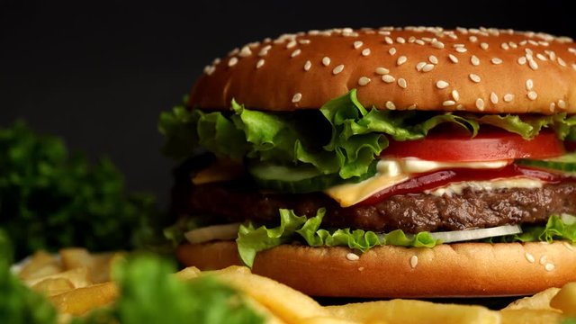 Big appetizing burger with meat cutlet, onion, vegetables, melted cheese, lettuce and mayonnaise sauce. Isolated hamburger rotates on dark smoke background, close-up view