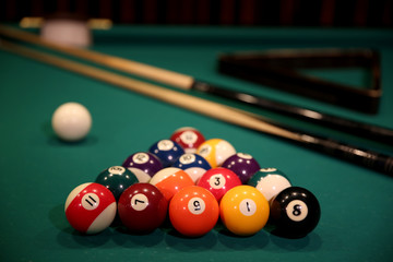 Sports game of billiards on a green cloth. Multi-colored billiard balls in the form of a triangle with numbers, two cues, a cue ball and a triangle on a pool table. Billiards billiard balls close up.