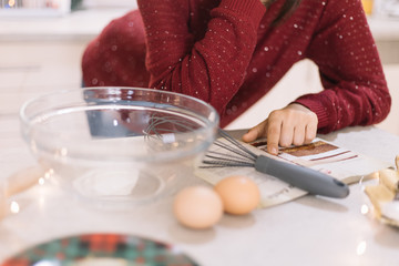 Woman's finger pointing recipe in book on kitchen bar