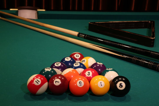 Sports game of billiards on a green cloth. Multi-colored billiard balls in the form of a triangle with numbers, two cues, a cue ball and a triangle on a pool table. Billiards billiard balls close up.