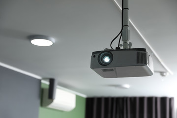 Modern video projector on ceiling in room