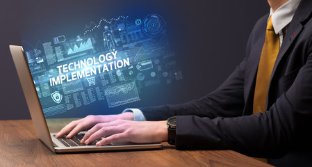 Businessman working on laptop with TECHNOLOGY IMPLEMENTATION inscription, cyber technology concept