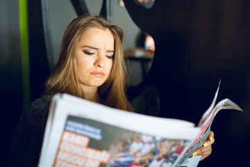 Portrait of young beautiful woman girl reading news papers sitting at home or at the cafe reacting...
