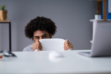 Frightened Young Businessman Hiding Behind Chair