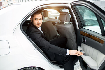 Fototapeta na wymiar handsome caucasian man with beard wearing tuxedo look side while closing the door of white car