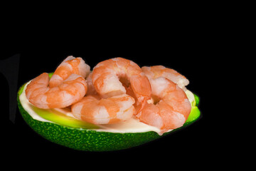 A dish, meal of half fresh avocado and peeled shrimp isolated on black background. Tasty healthy food with vegetables and seafood, low kea.
