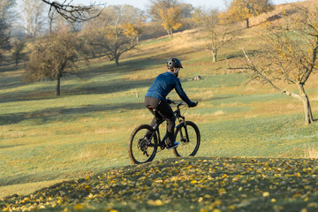 Naklejka premium Cyclist in pants and fleece jacket on a modern carbon hardtail bike with an air suspension fork rides off-road. 