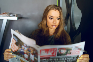 Fototapeta premium Young girl woman sitting at the cafe or restaurant or at home holding and reading newspapers reacting to the article news making faces
