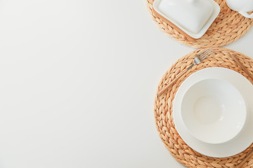 White ceramic tableware, fibre braided round placemat and cutlery set on white background. Scandinavian style.