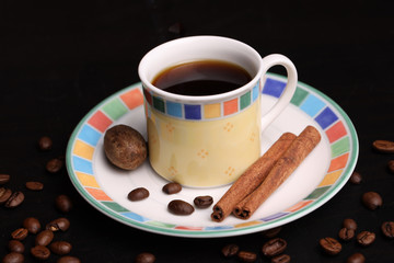 cup of coffee on saucer garnished with cinnamon sticks and nutmeg