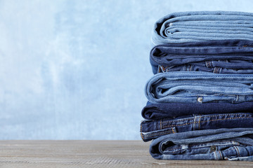 Stack of different jeans on wooden table against blue background. Space for text